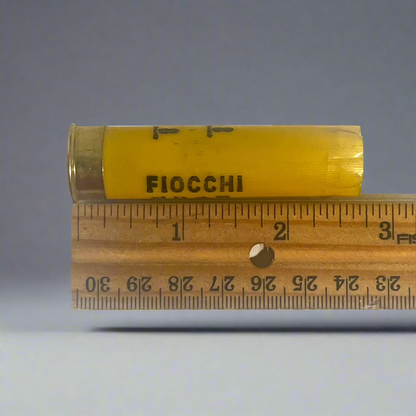 Yellow Fiocchi shotgun shell hull measured on a wooden ruler at approximately 2.75 inches