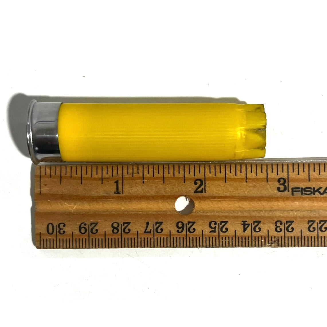 A yellow shotgun shell with silver base measured against a Fiskars ruler showing about 2.7 inches