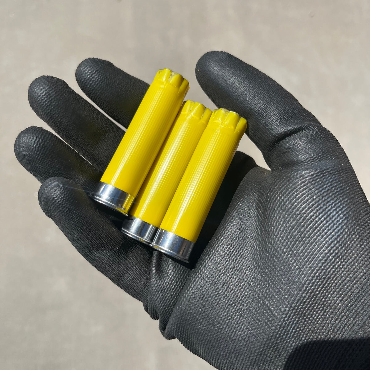 A gloved hand holding 3 yellow shotgun shells with silver bases