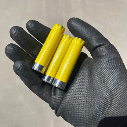 A gloved hand holding 3 yellow shotgun shells with silver bases