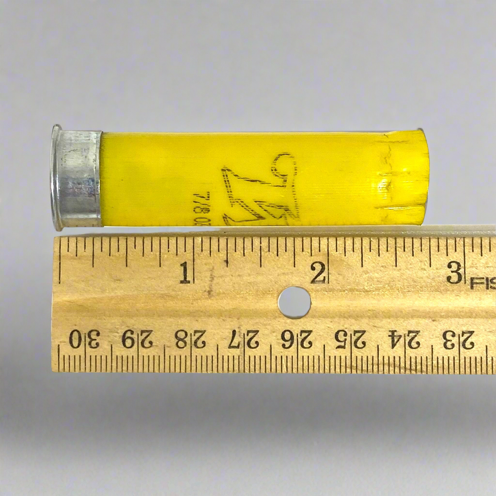 A yellow shotgun shell with a silver bottom beside a ruler showing a length of about 2.75 inches