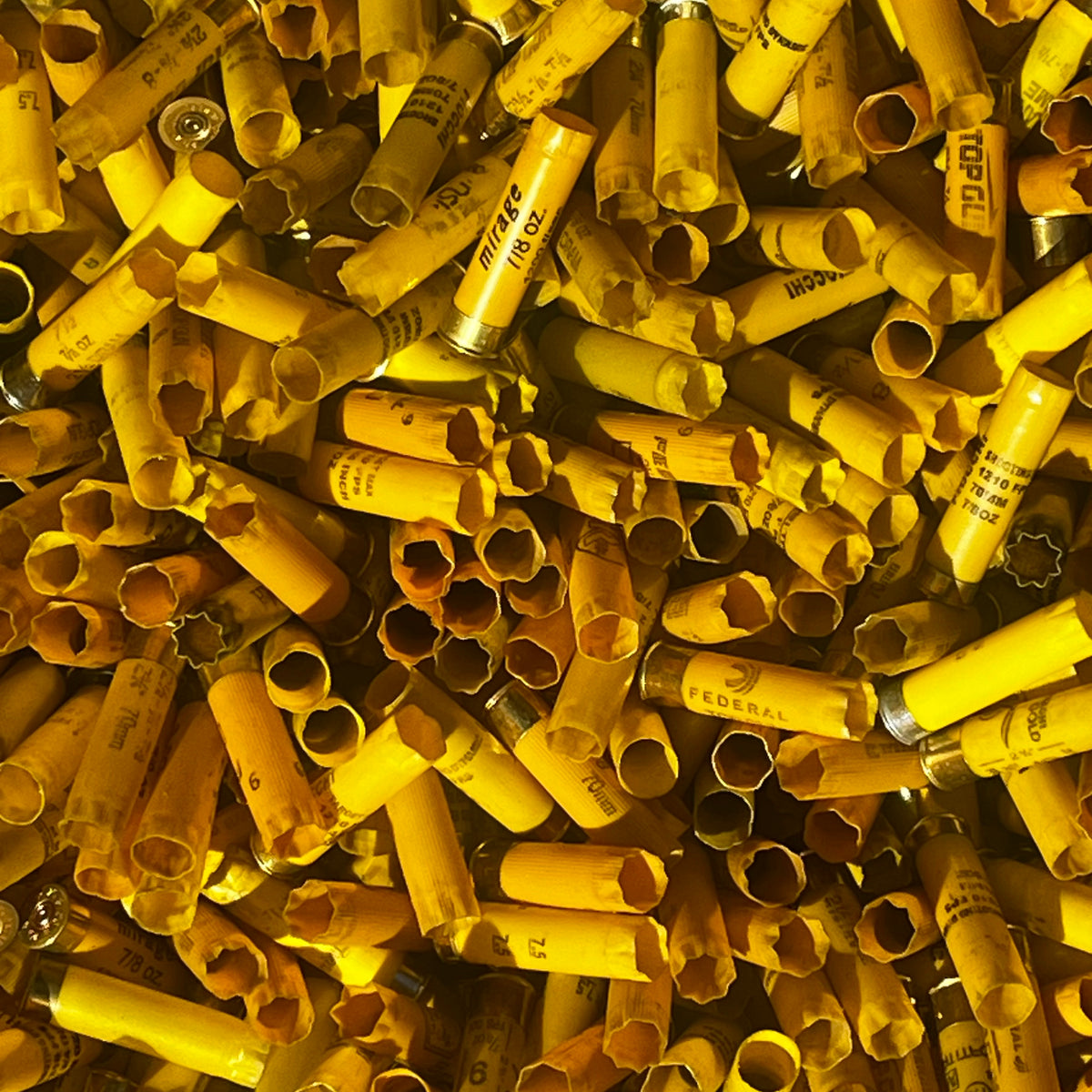 Close-up of a large pile of mixed yellow shotgun shell hulls with open mouths and visible brand markings