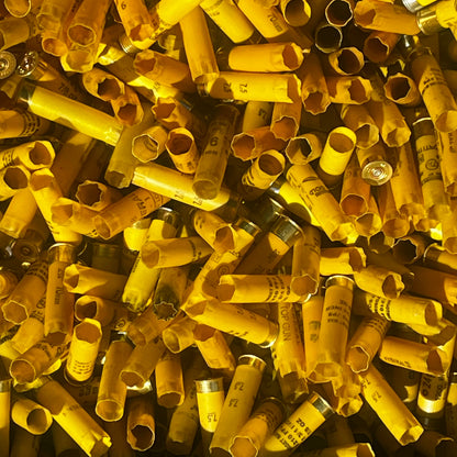 Close-up of a large pile of mixed yellow shotgun shell hulls with open mouths, some showing gauge numbers
