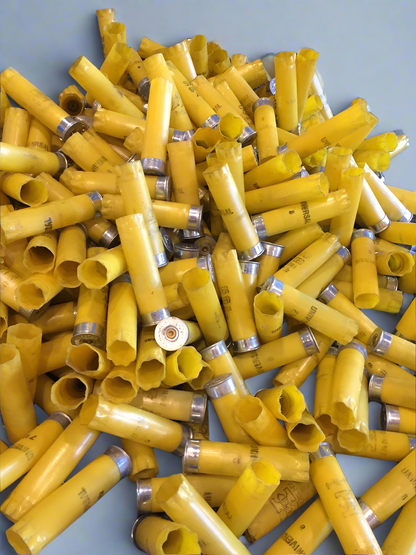 A large pile of yellow shotgun shell hulls with silver bottoms on a gray surface