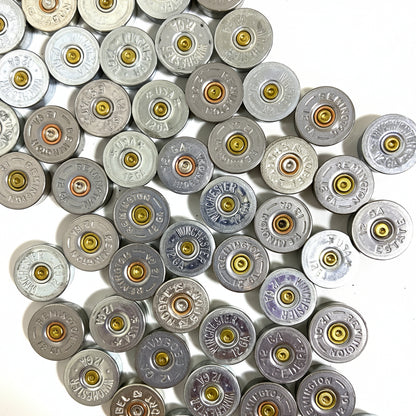 Silver 12 gauge shotgun shell end caps packed edge-to-edge, showing mixed headstamp markings.