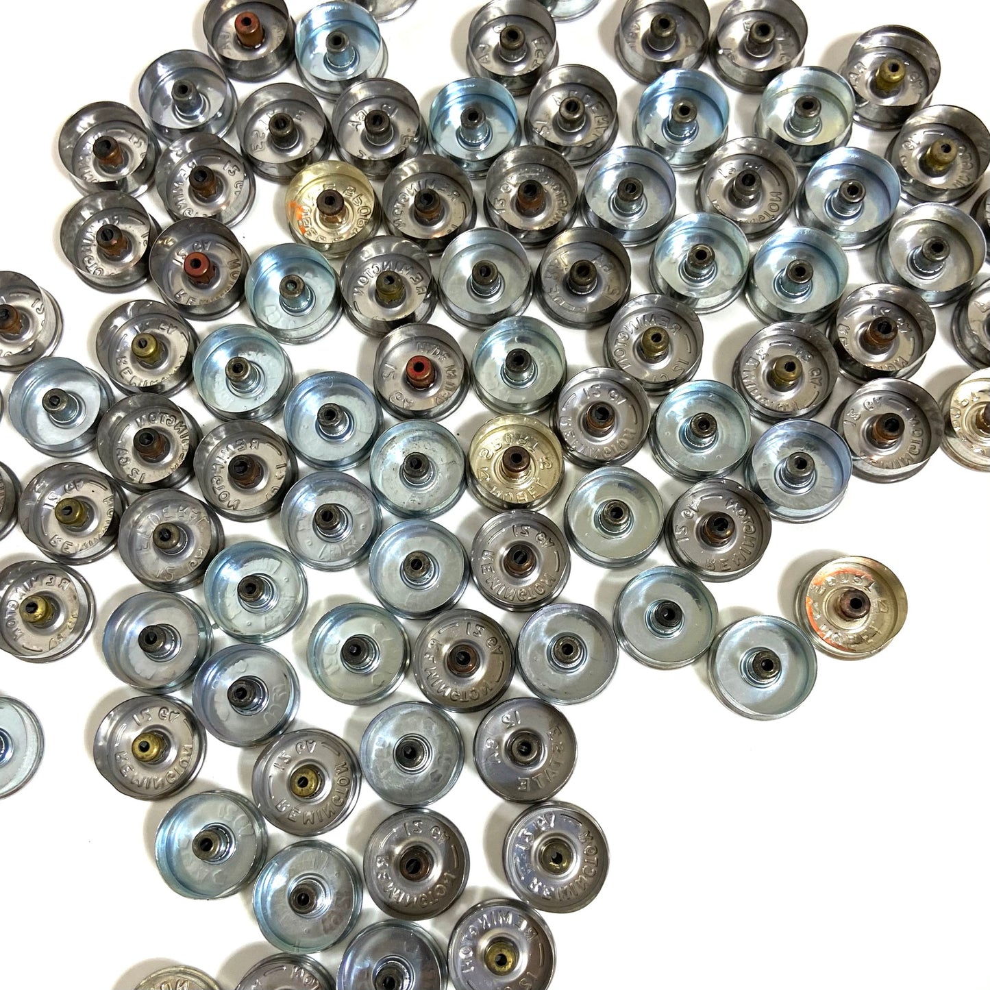 Silver 12 gauge shotgun shell bottoms shown from the inside, scattered together with a few gold-toned pieces.