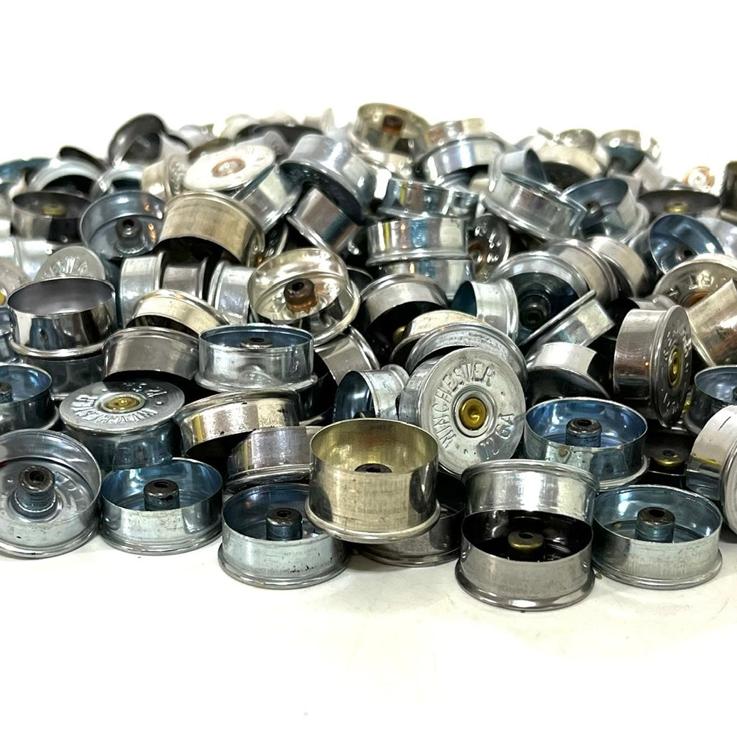 Silver 12 gauge shotgun shell bottoms heaped together, mixed finishes and manufacturer markings.