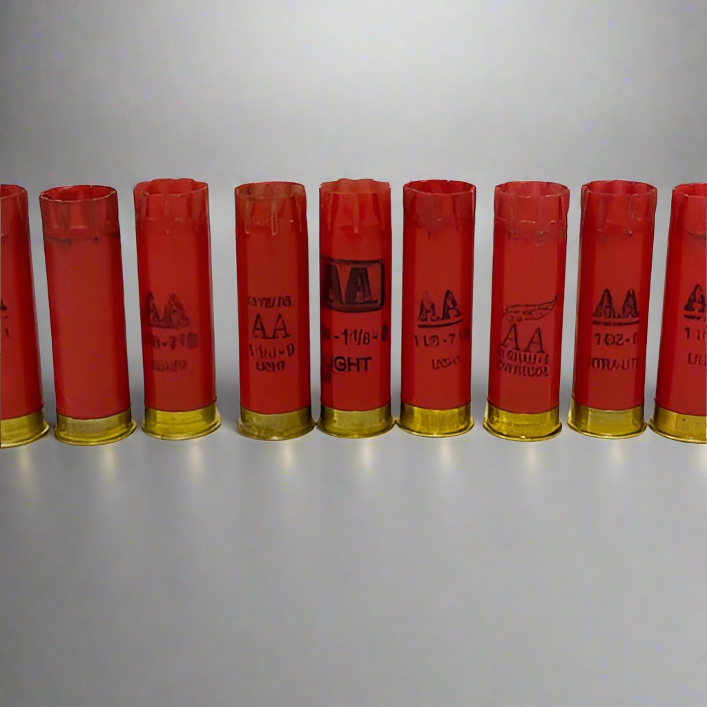 Group of red 12 gauge empty shotshells standing upright with gold-colored brass ends resting on white surface.