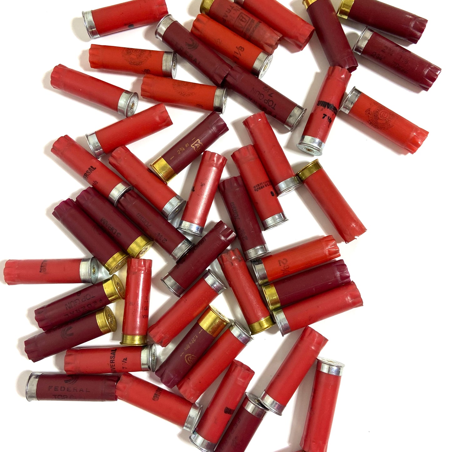 Jumbled pile of mixed red and burgundy empty hulls with silver and gold bases scattered on a white surface for crafting.