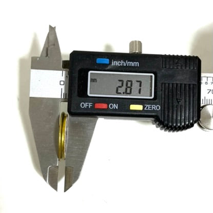 Digital caliper measuring the slice thickness of a 12 gauge shotgun shell headstamp slice showing 2.87 mm.