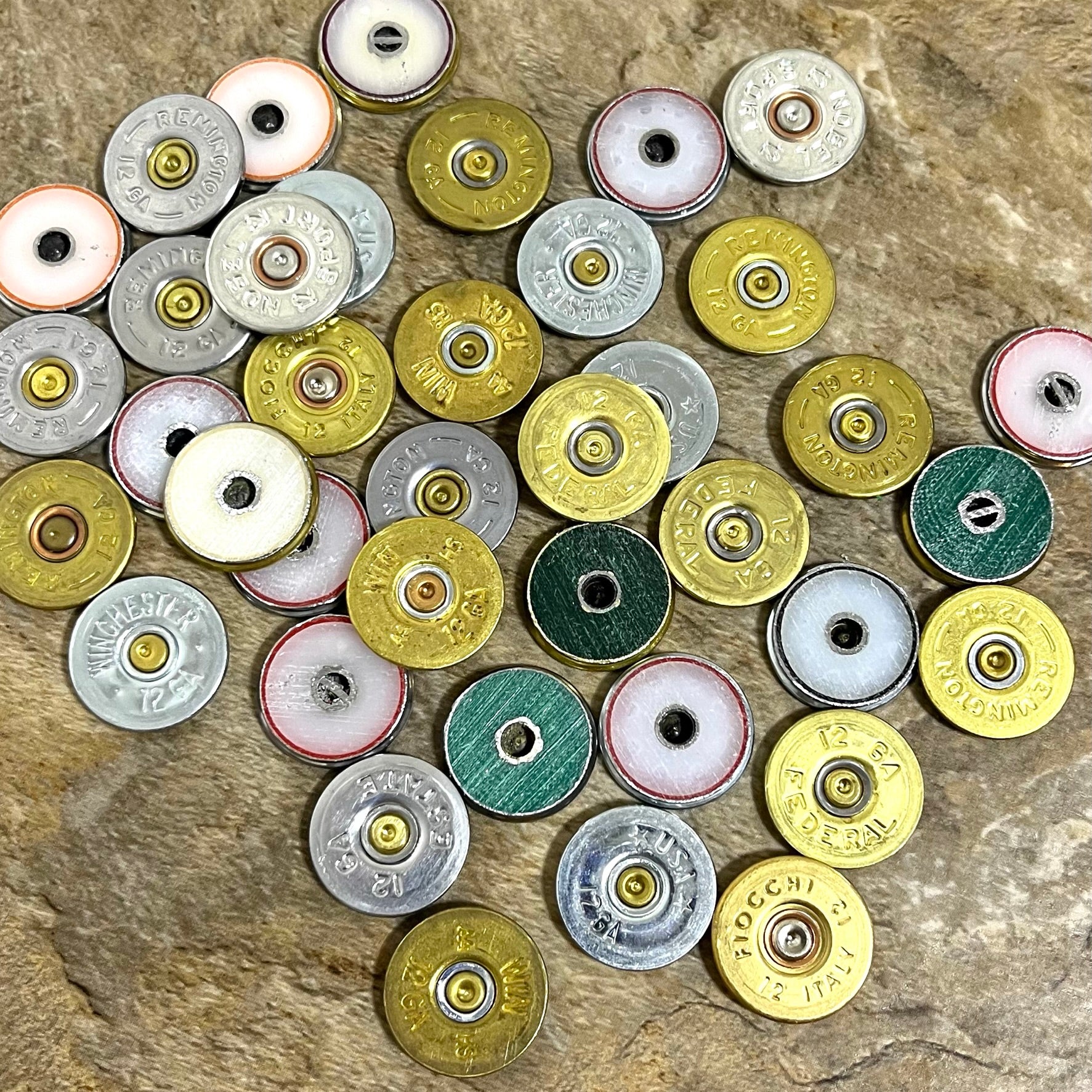 Assorted 12 gauge shotgun shell slices on a stone background showing colored primer center inserts.