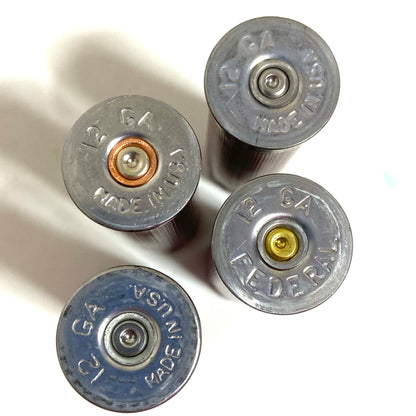 Close-up of four silver headstamps on 12 gauge empty shotgun shells showing 12 GA and MADE IN USA text.
