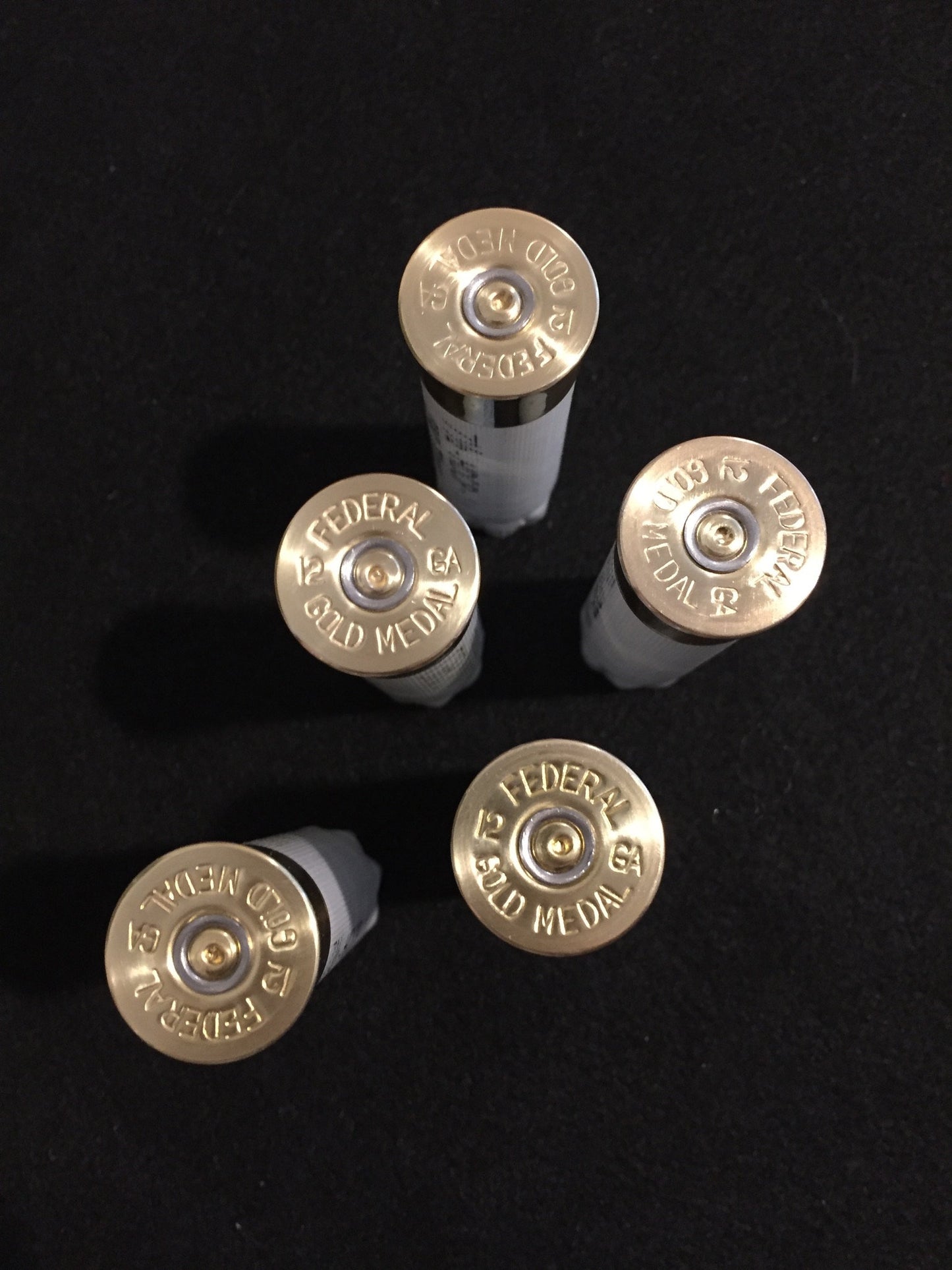 Bottom view of five white 12ga empty shells showing the gold brass heads stamped with Federal Gold Medal against a dark background.