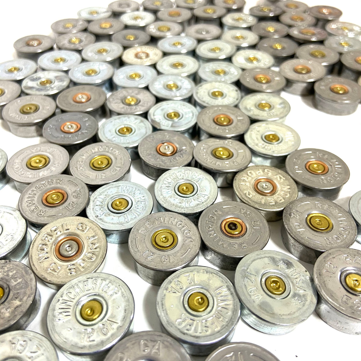 Silver 12 gauge shotgun shell end caps arranged in diagonal rows on white background, mixed brands.