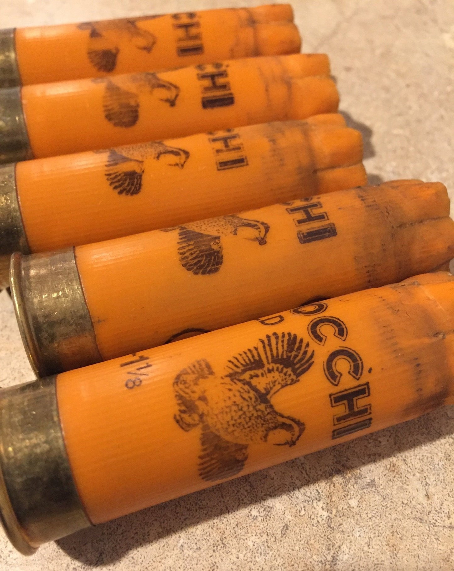 Five orange 12 gauge empty cartridges with printed pheasant graphics lying flat on a light beige stone surface.