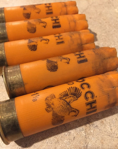 Five orange 12 gauge empty cartridges with printed pheasant graphics lying flat on a light beige stone surface.