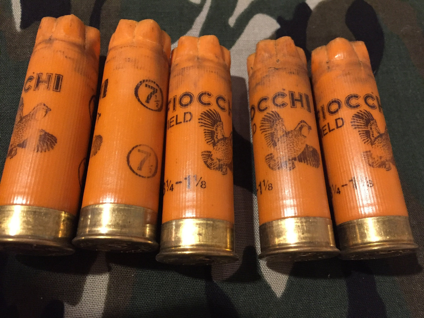 Five orange 12 gauge empty shotshells with printed pheasant graphics standing in a row on a camouflage background.