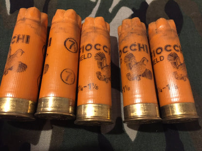 Five orange 12 gauge empty shotshells with printed pheasant graphics standing in a row on a camouflage background.