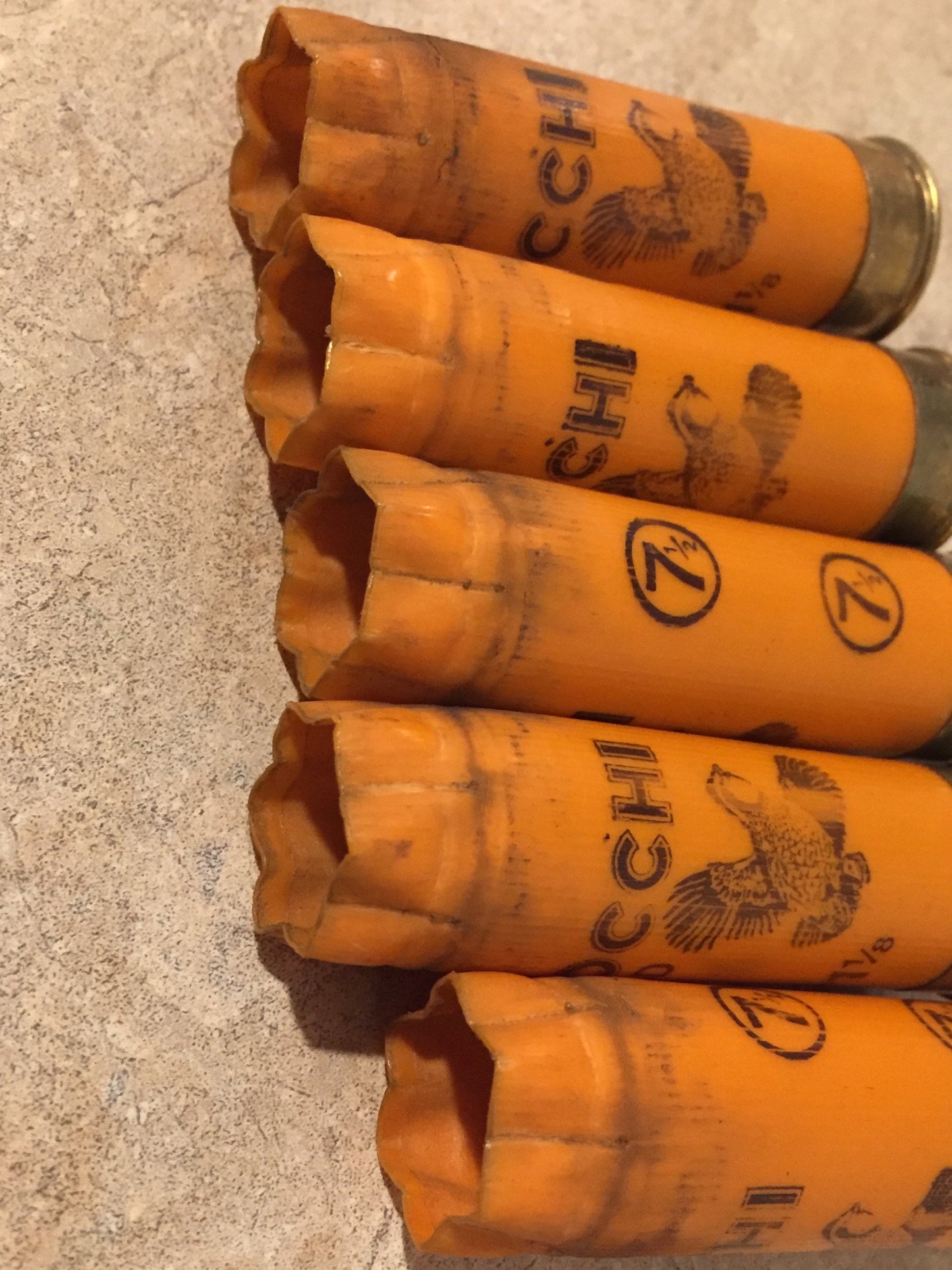 Five orange 12 gauge once-fired shells on a stone surface showing open crimped ends, printed pheasants, and shot text.