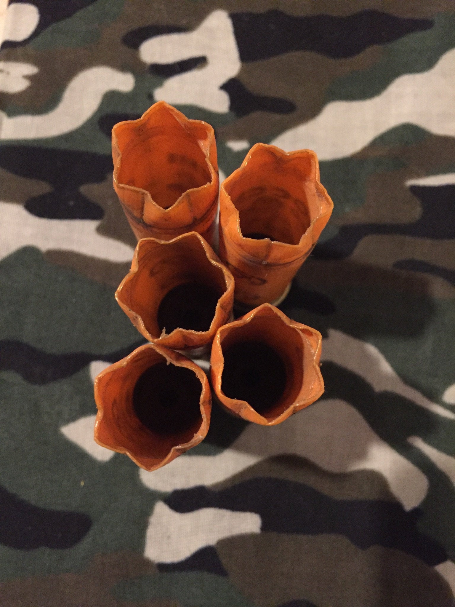 Overhead view looking into five hollow open mouths, crimps of orange 12 gauge shotshell hulls clustered on camouflage fabric.