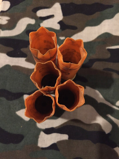 Overhead view looking into five hollow open mouths, crimps of orange 12 gauge shotshell hulls clustered on camouflage fabric.