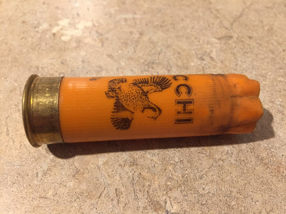 One horizontal orange 12 gauge shotshell with printed pheasant graphic lying on a speckled stone surface.