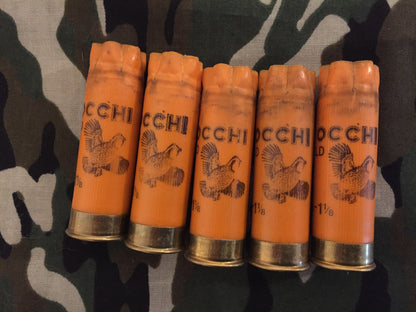 Five orange 12 gauge spent casings standing in a row on camouflage fabric, showing top crimped ends and pheasant print.