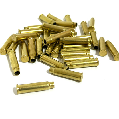 A pile of empty .17 HMR brass casings on a white background with one single case lying in the foreground.