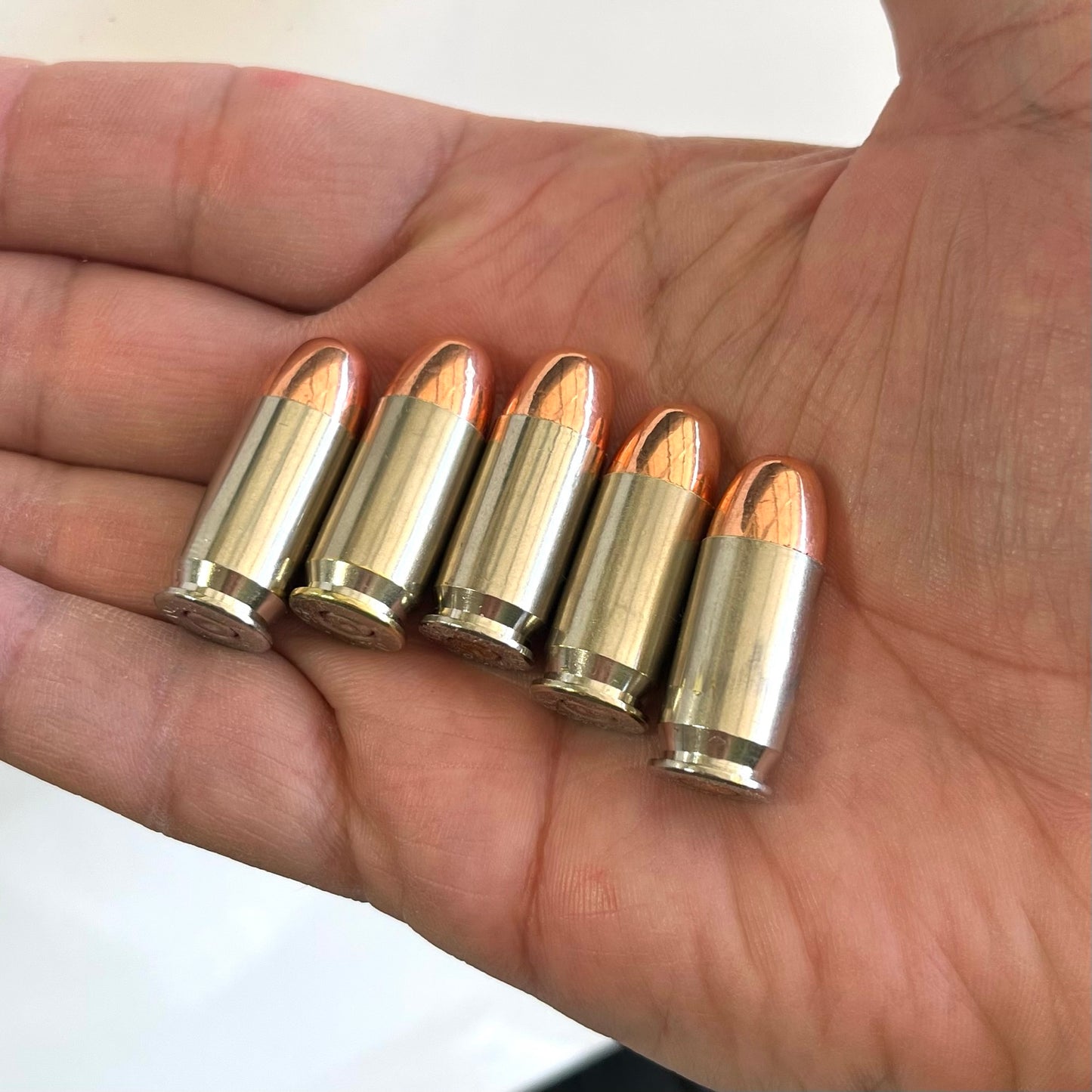 Five nickel snap caps with copper round nose bullets sitting in an open human hand.