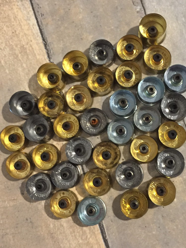 Pile of 20 gauge spent shotgun shell bottoms in two-tone metallic finishes.
