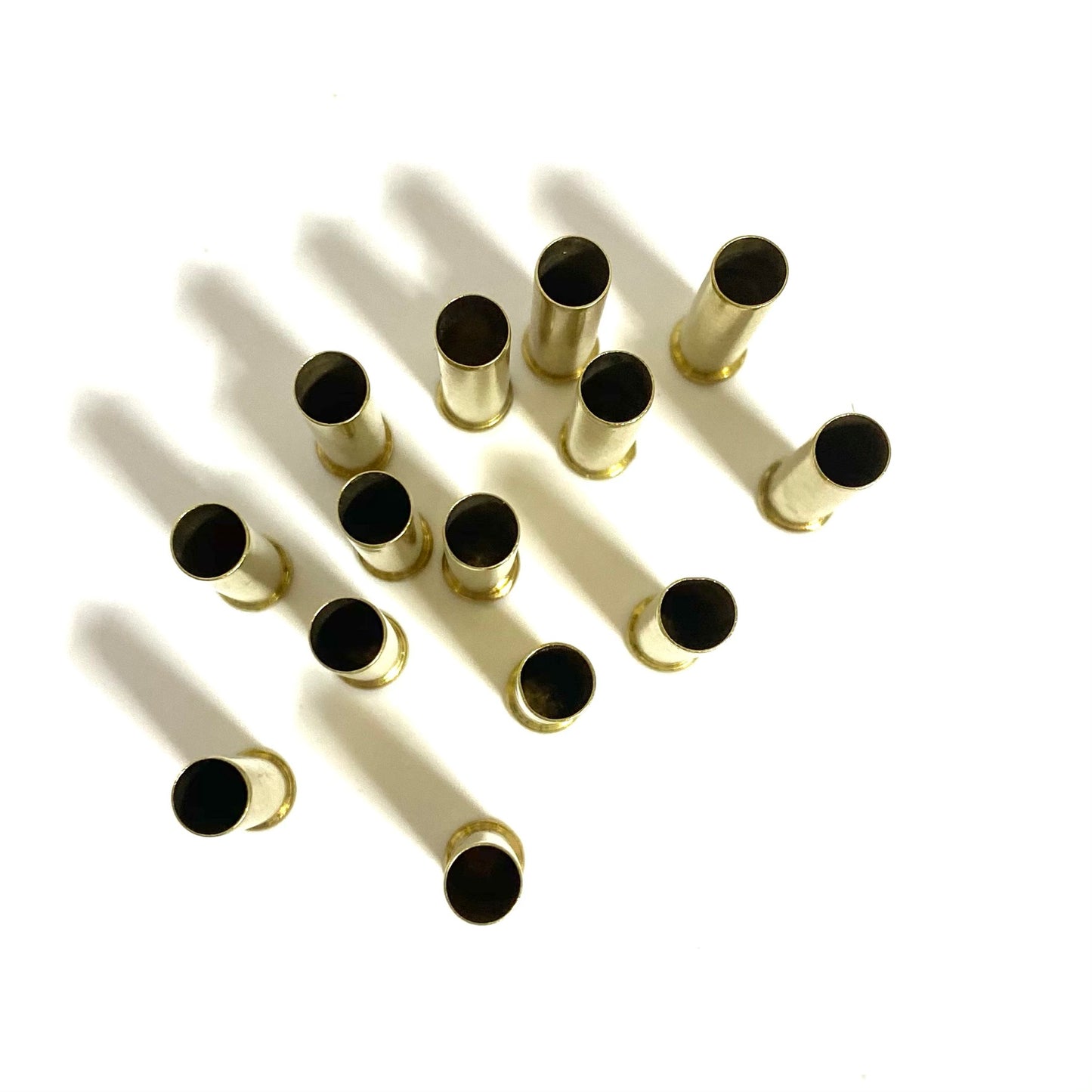 Twelve .22 WMR brass casings standing upright on white showing open mouths and long shadows.