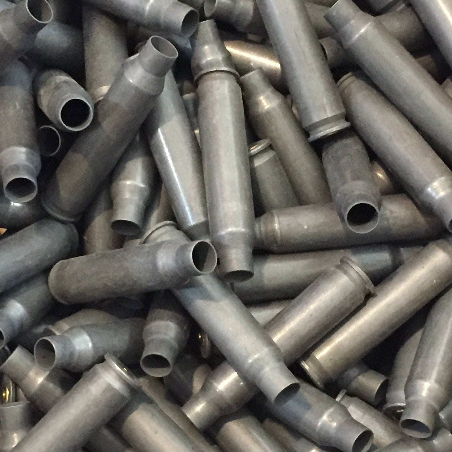 A large pile of once-fired gray steel .223/5.56 casings lies tangled together, showing open mouths and rims.