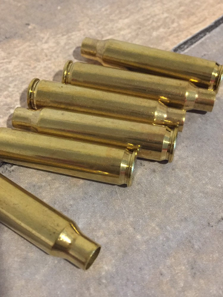 Five polished brass 223 5.56 empty spent bullet casings lying on a tile floor