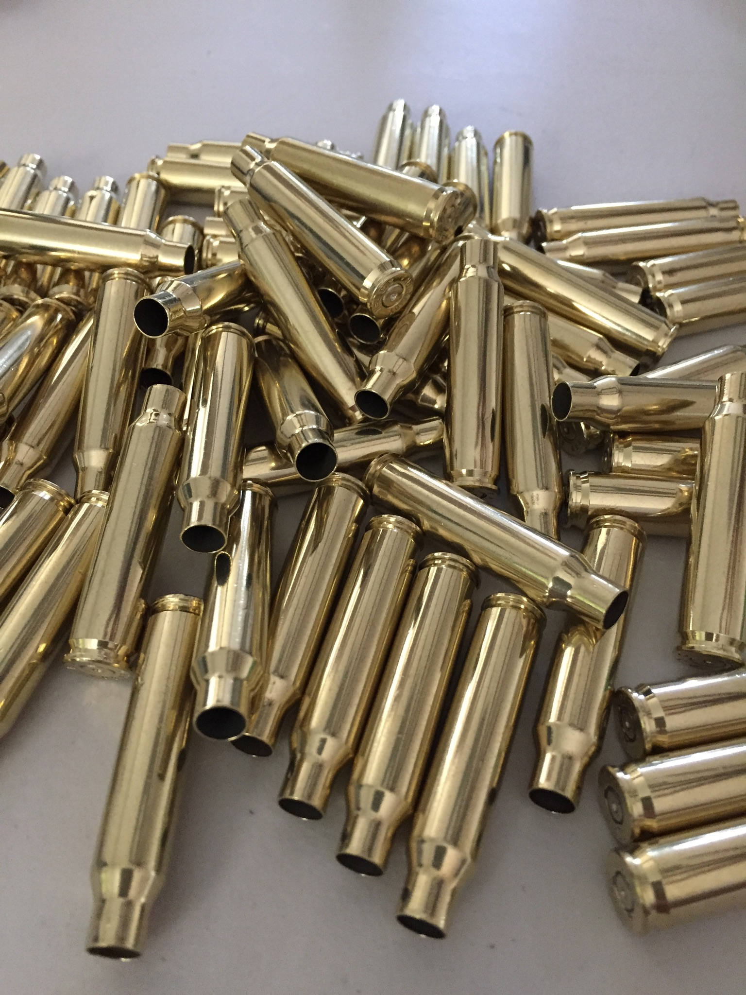 A pile of polished brass 223 5.56 empty spent bullet casings on a gray surface