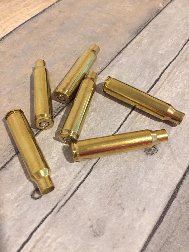 Six polished brass 223 5.56 empty spent bullet casings scattered on a wood plank surface