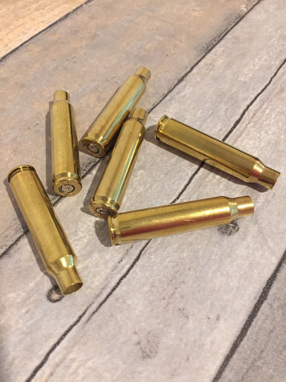 Six polished brass 223 5.56 empty spent bullet casings scattered on a wood plank surface