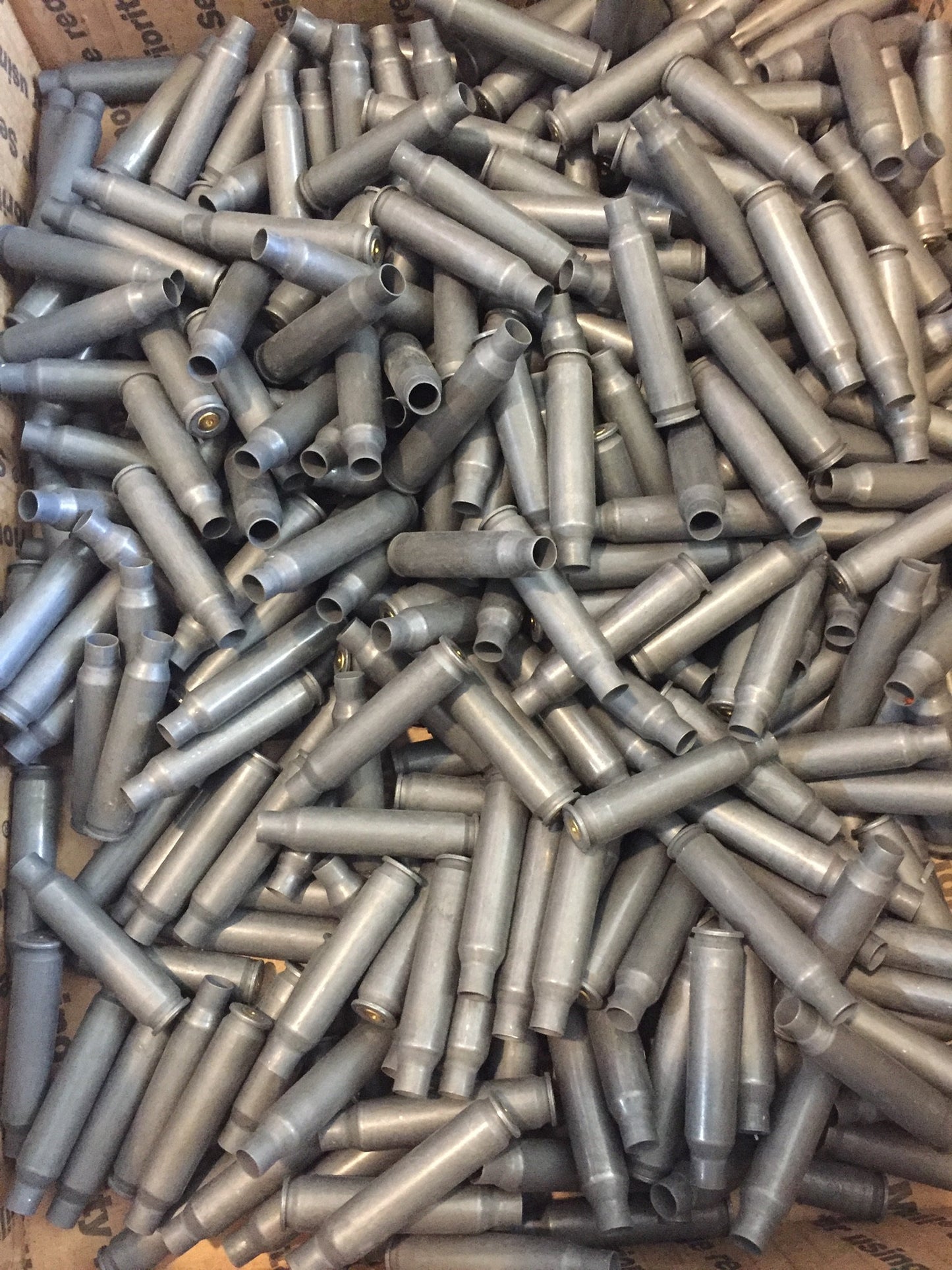A large bulk pile of spent gray steel shells fills a cardboard box, tangled together.