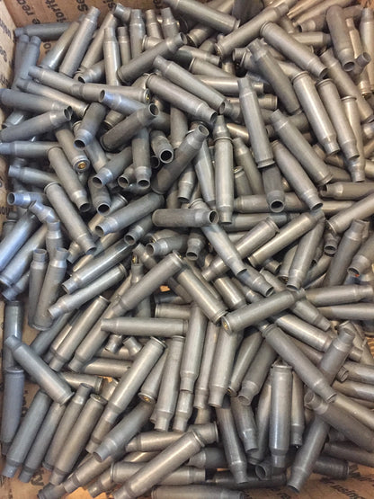A large bulk pile of spent gray steel shells fills a cardboard box, tangled together.