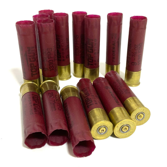28 gauge dark red Federal casings, some standing with open mouths and others lying showing brass primers