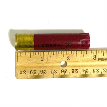 Single 28 gauge dark red Federal shell laid on a wooden ruler, showing its length near three inches