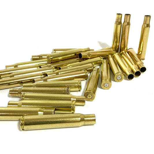 A pile of empty 30-06 POLISHED brass shells scattered on a clean white surface with several casings standing upright.
