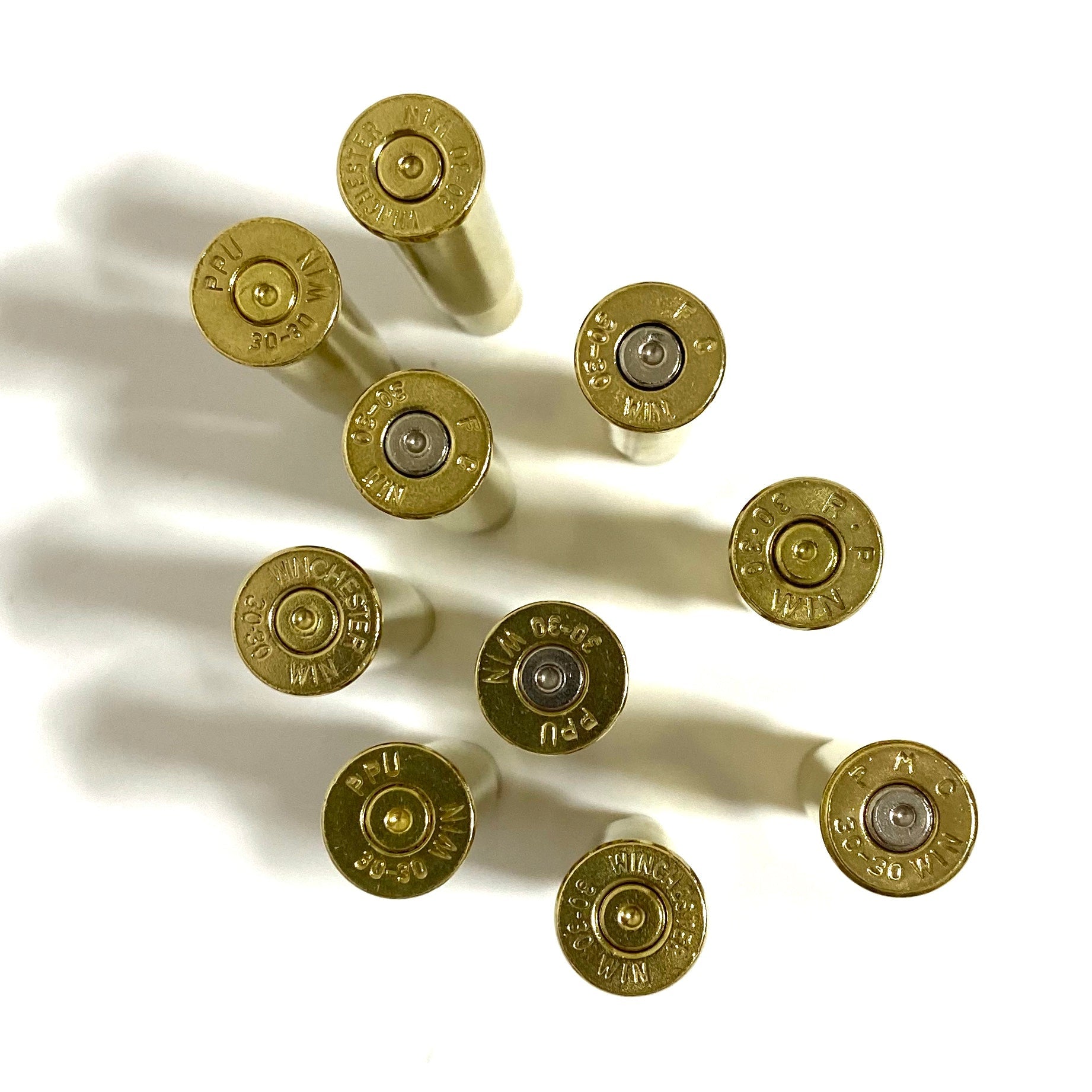 Top-down view of 30-30 brass headstamps and spent inert primers, mixed silver and gold primers, polished shine.
