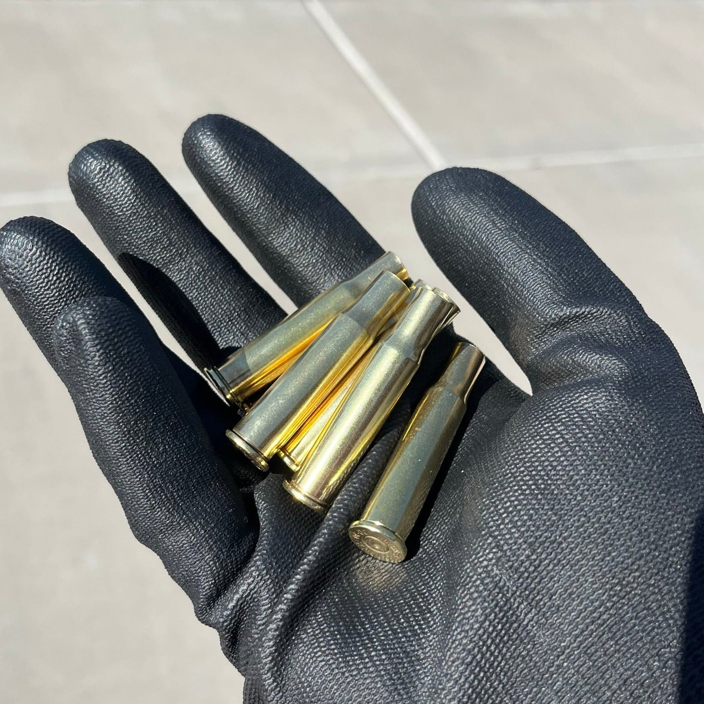 Black gloved hand holding five polished 30-30 Winchester brass casings, bright gold shine, once-fired empty shells.
