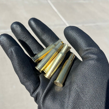 Black gloved hand holding five polished 30-30 Winchester brass casings, bright gold shine, once-fired empty shells.
