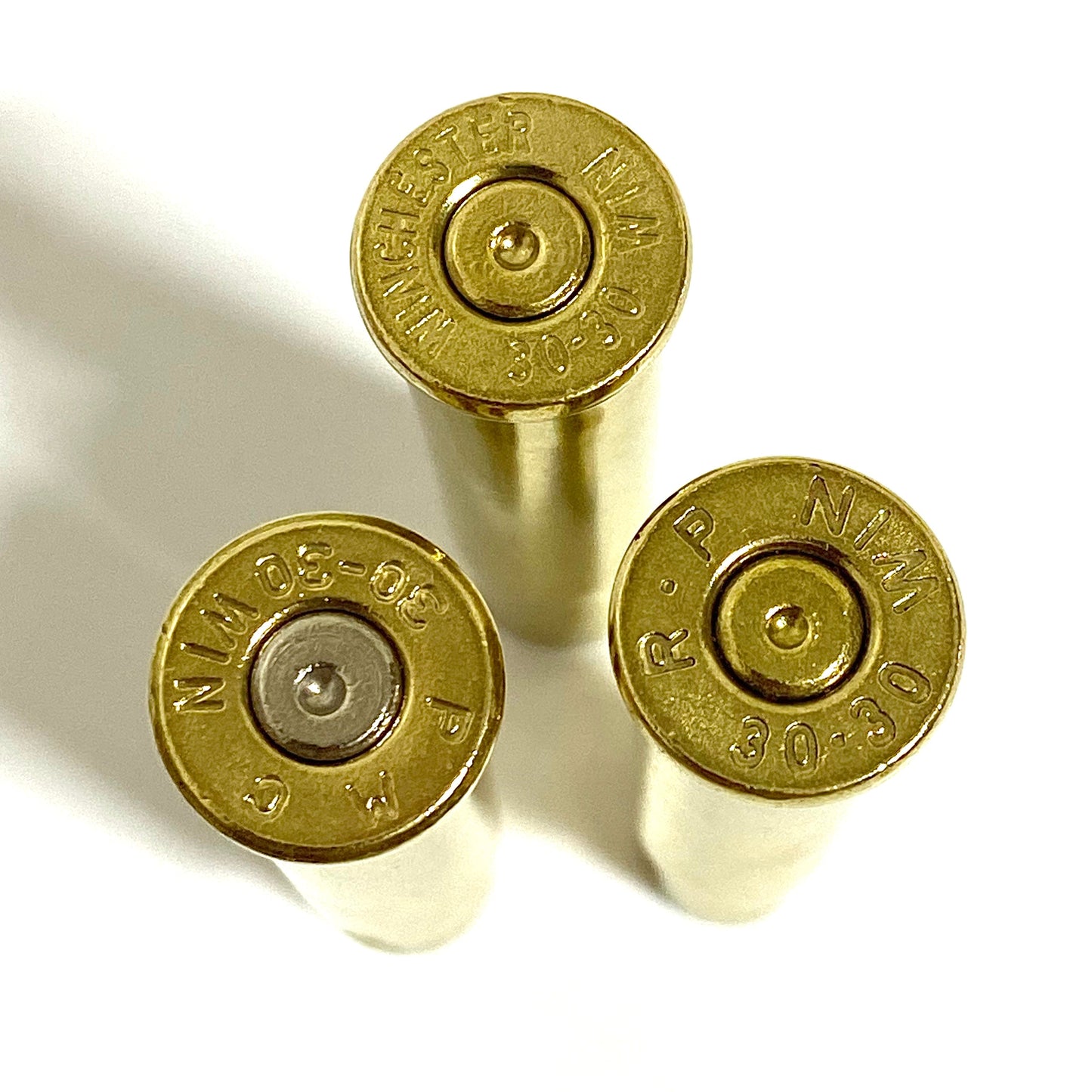 Extreme close-up of three 30-30 brass casings, showing clear headstamps, spent primers, and tumbled gold finish.
