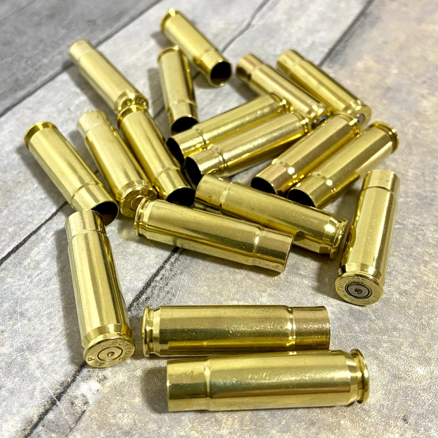 Shiny gold 300 Blackout spent brass rifle casings scattered across a textured grey surface.