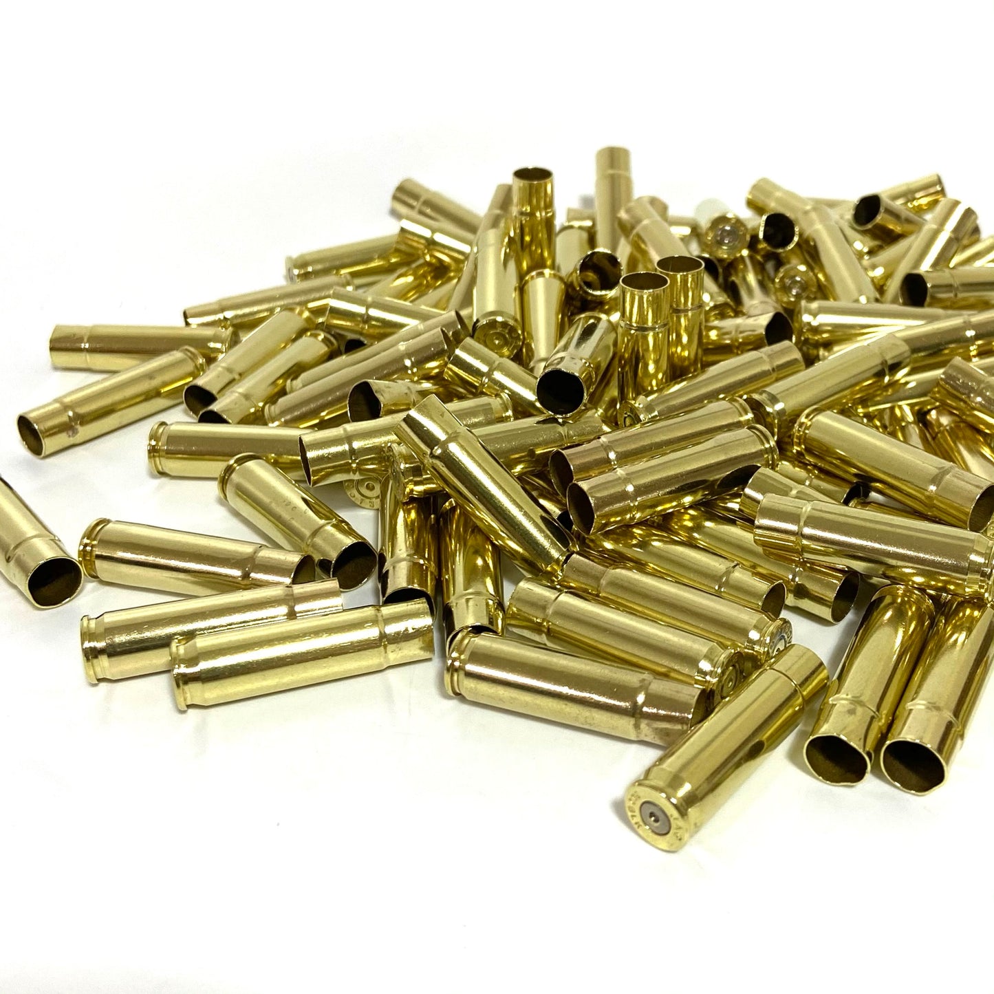 A large pile of shiny empty 300 Blackout brass rifle shell casings scattered on a white surface.