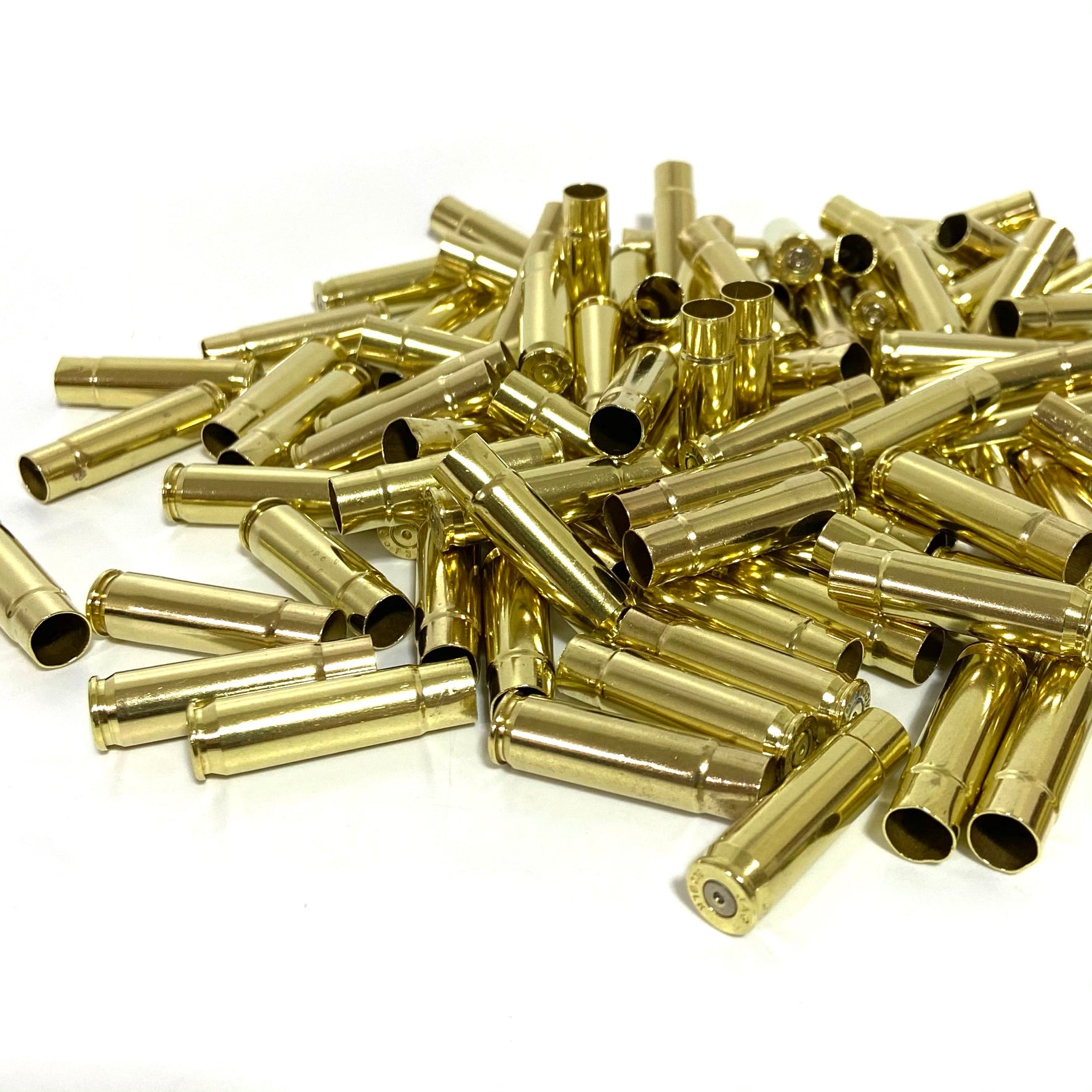 A large pile of shiny empty 300 Blackout brass rifle shell casings scattered on a white surface.