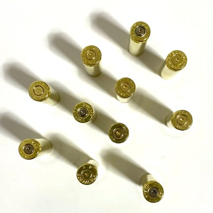 Nine empty 300 Blackout recycled brass casings standing upright and casting shadows on a white surface.