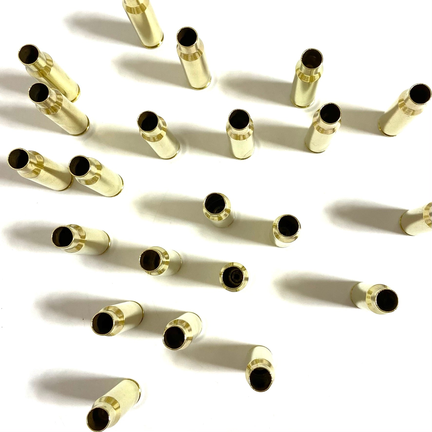Top view 15 gold 308 WIN brass cases scattered across a white background, displaying open case mouths and soft shadows.